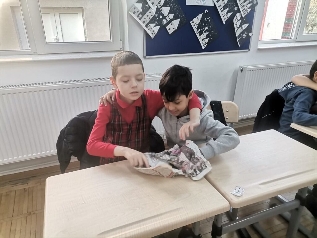Doi băieți așezați în bancă, în clasă, împărțind un sandviș